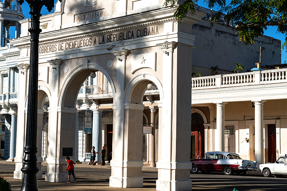 Memorial arch of Parque Jose Marti in dappled morning light, boy in red playing hide and seek, Cienfuegos, Cuba