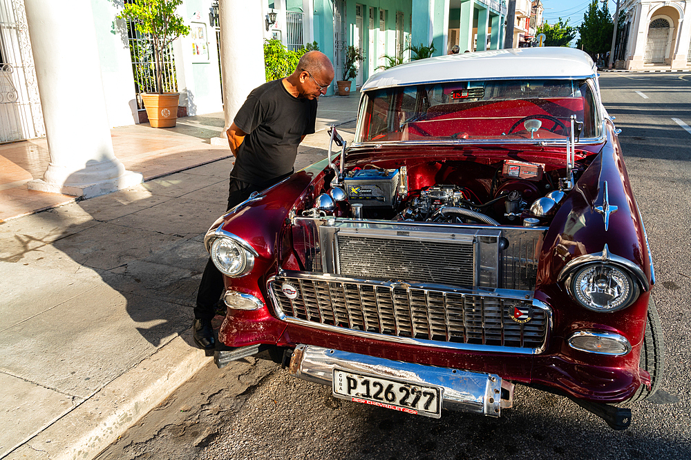 Cuban man inspecting and admiring the open engine of a red classic Chevrolet car, Cienfuegos, Cuba (Model release