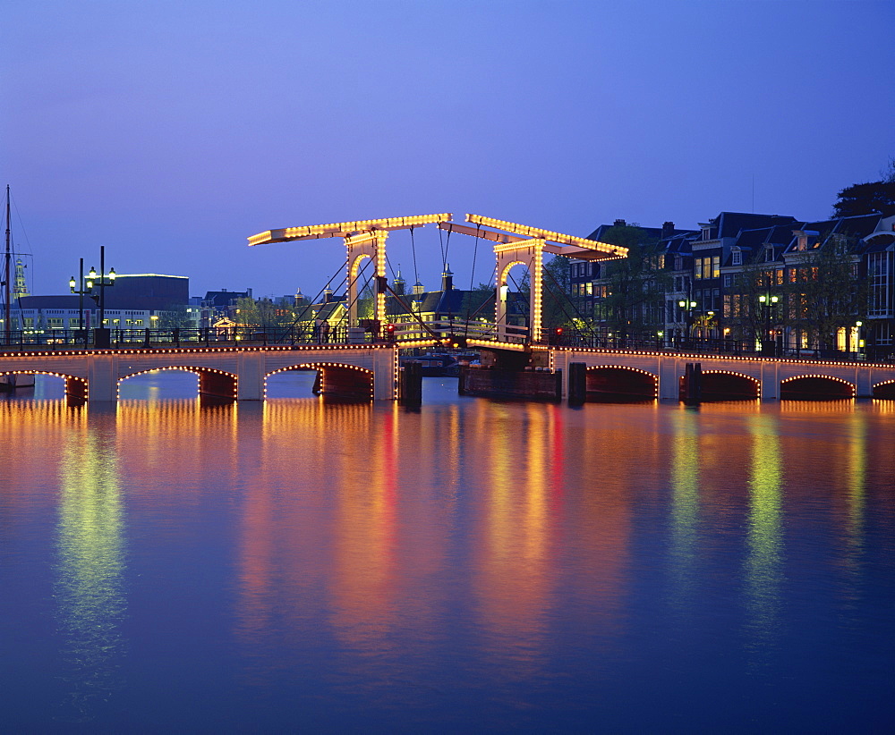 Lights on the Magere Brug (Skinny Bridge), reflected in the canal in the evening in Amsterdam, Holland, Europe