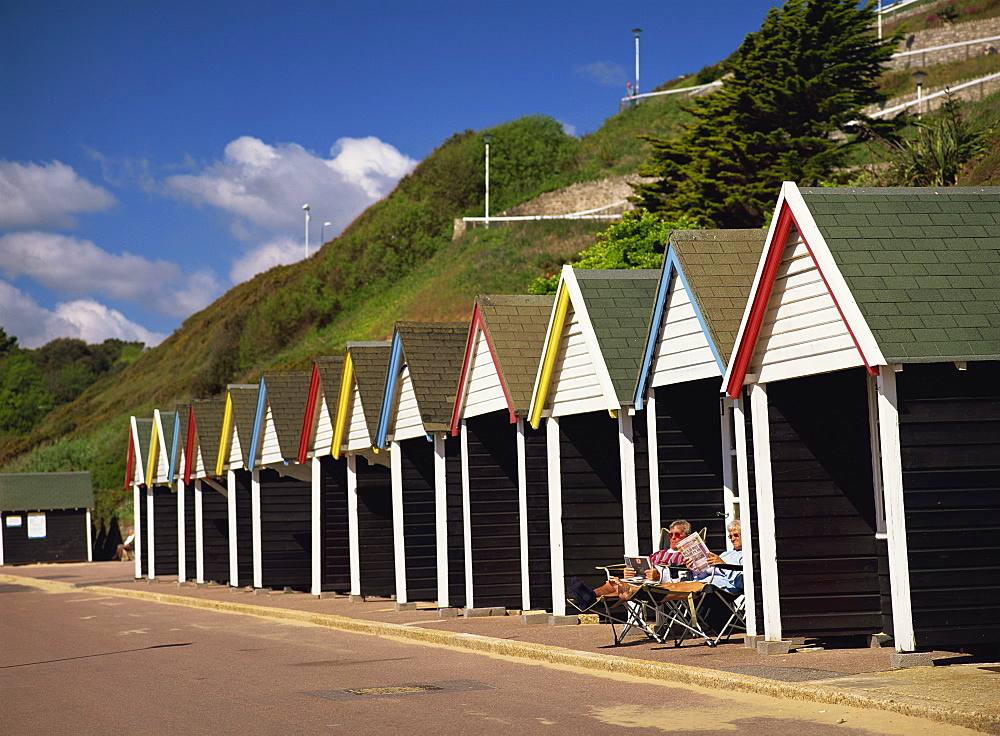 Relaxing on the Promenade outside a colourful beach hut below the cliff in early summer sunshine. West Cliff, Bournemouth, Dorset, England, United Kingdom, Europe