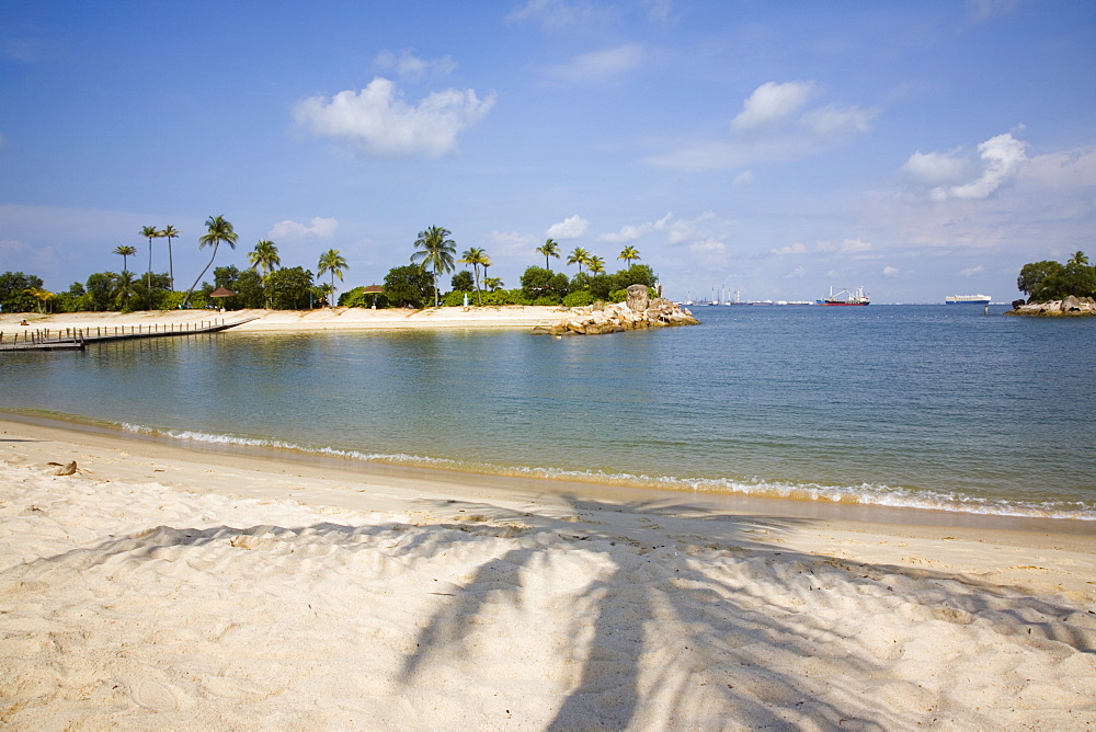 Empty sheltered tropical Siloso beach and bay, palm tree shadow on imported sand with man-made island at western end of southern coast, Sentosa Island, Singapore, Southeast Asia, Asia