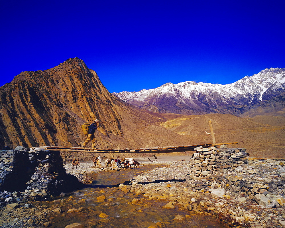 Nepalese man on a bridge crossing a stream in the Kangaki River Valley, near KaGBeni, Southern Mustang, Nepal