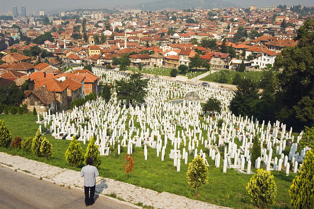 Man reflecting at cemetery overlooking city houses, Sarajevo, Bosnia, Bosnia-Herzegovina, Europe