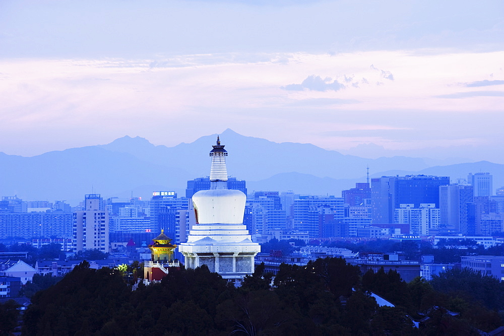 An illuminated White Pagoda and city buildings at sunset, Beihai park, Beijing, China, Asia