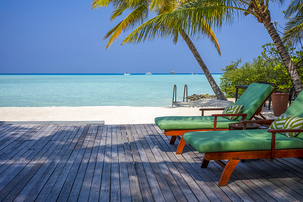 Two sunbeds in the shade overlooking the crystal clear lagoon on an exotic Island in the Maldives. Indian Ocean.