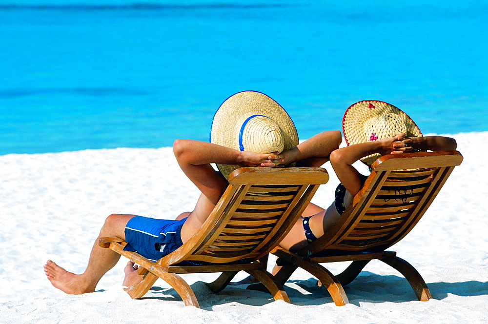 Couple lying in deck chairs on beach, The Maldives, Indian Ocean, Asia