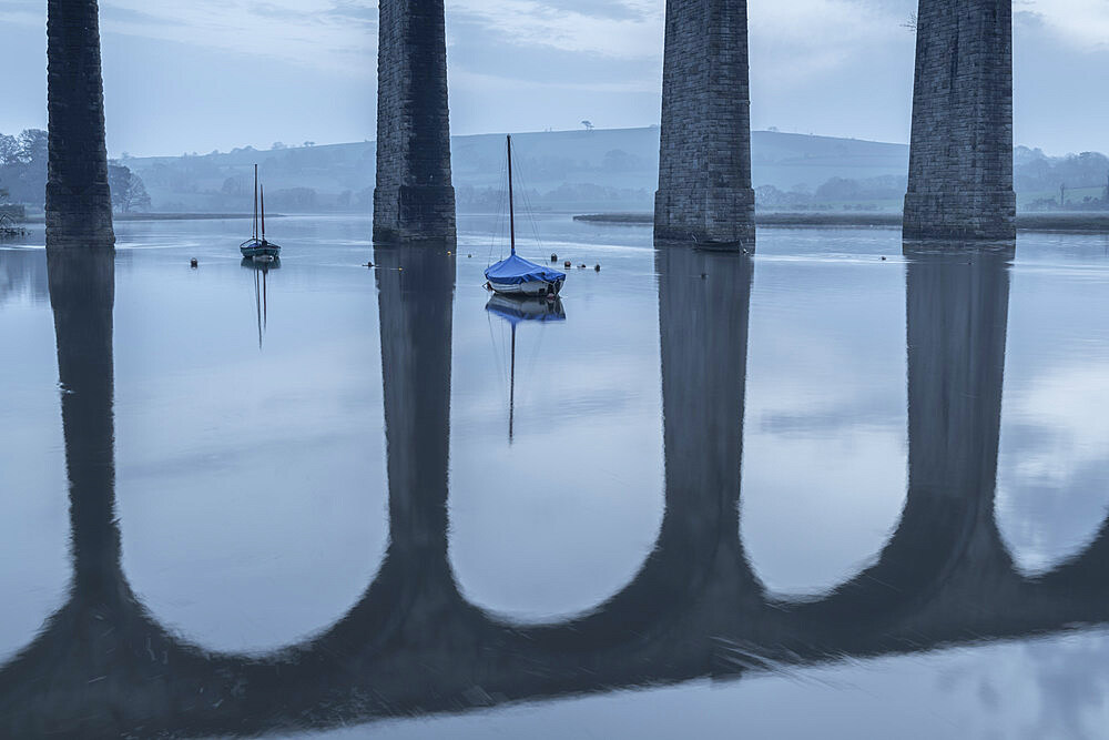 Boats moored beneath the towering arches of St. Germans viaduct over the River Tiddy at dawn in spring, St. Germans, Cornwall, England, United Kingdom, Europe