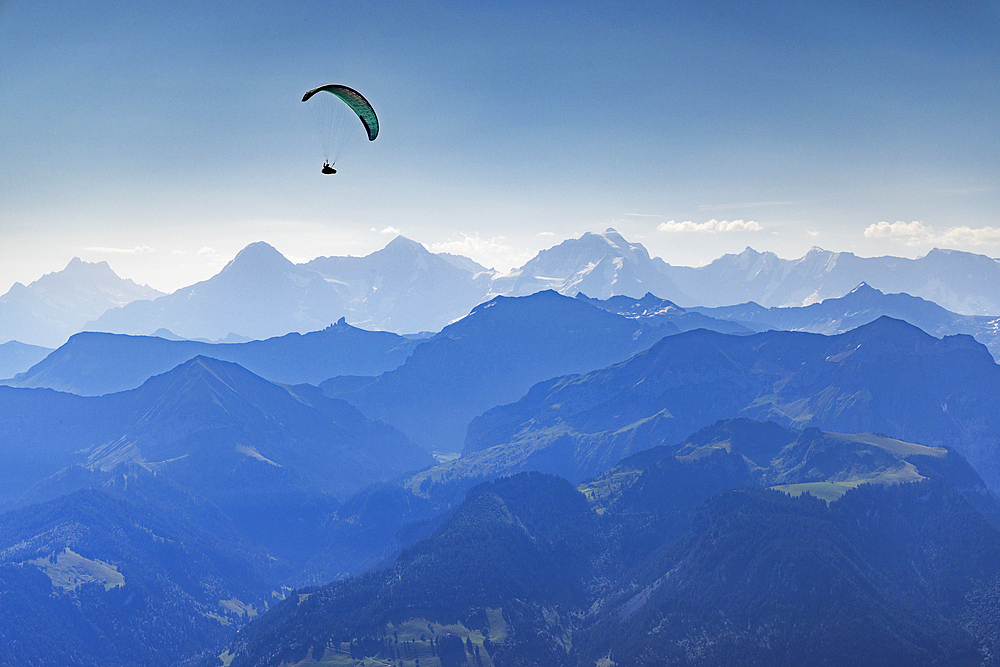 Paraglider flying over Kander Valley with Jungfrau, Monch and Eiger mountains in the background, Canton of Bern, Switzerland