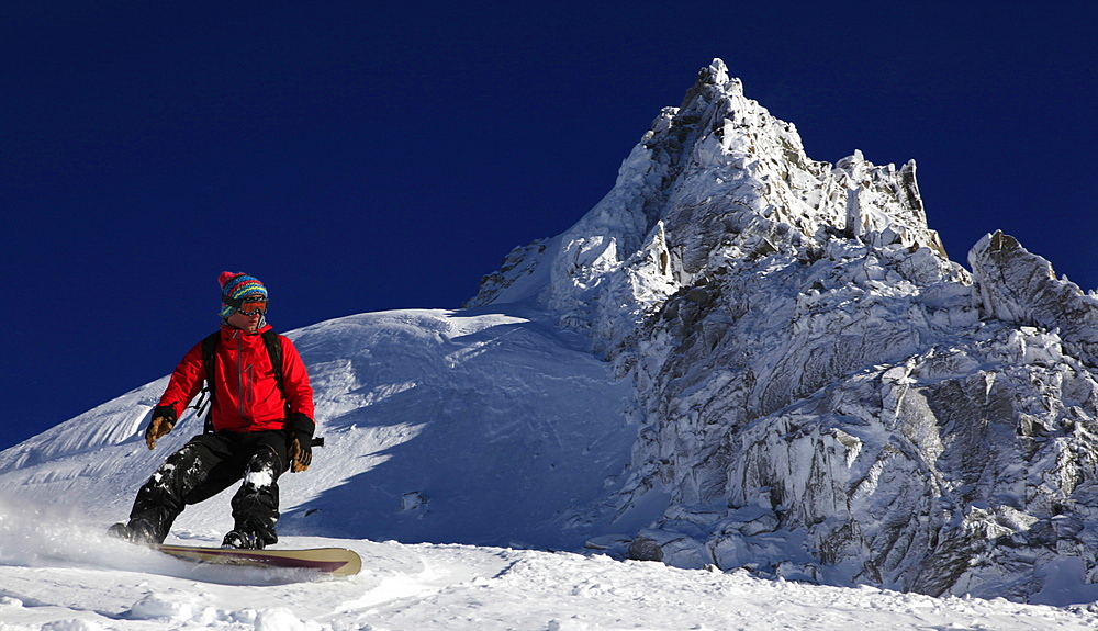 A snowboarder riding powder snow off the top of the famous Grand Montets ski area, high above Argentiere, Chamonix Valley, Haute Savoie, French Alps, France, Europe