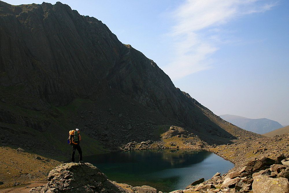 A hiker looks across the still waters of Llyn Du'r Arddu, one of Wales's highest lakes, which lies under cliffs below the Snowdon railway and the summit of Snowdon, Snowdonia, Wales, United Kingdom, Europe