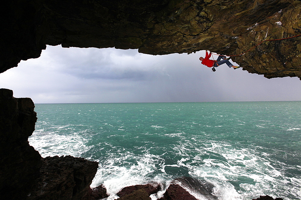 A climber scales a sea cave near Swanage, Dorset, England, United Kingdom, Europe