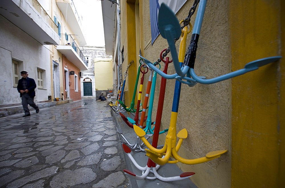 A local man walks past traditional Greek anchors for sale outside a chandler's store, Pothia Town, Kalymnos Island, Dodecanese, Greek Islands, Greece, Europe