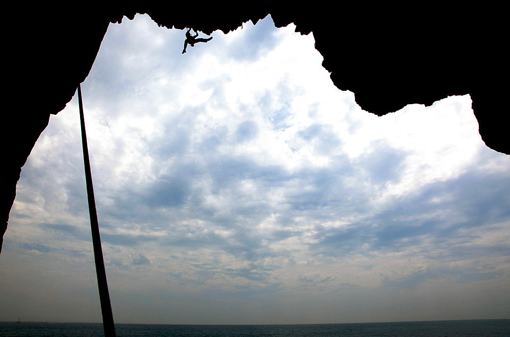 A climber scales a sea cave on cliffs near Swanage, Dorset, England, United Kingdom, Europe