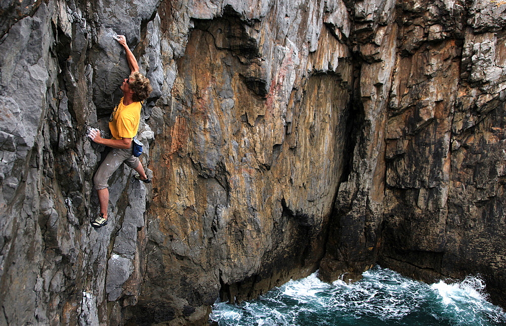 A climber deep water soloing above the sea on the limestone cliffs near St. Govan's Head, South Pembrokeshire, Pembrokeshire Coast National Park, Wales, United Kingdom, Europe