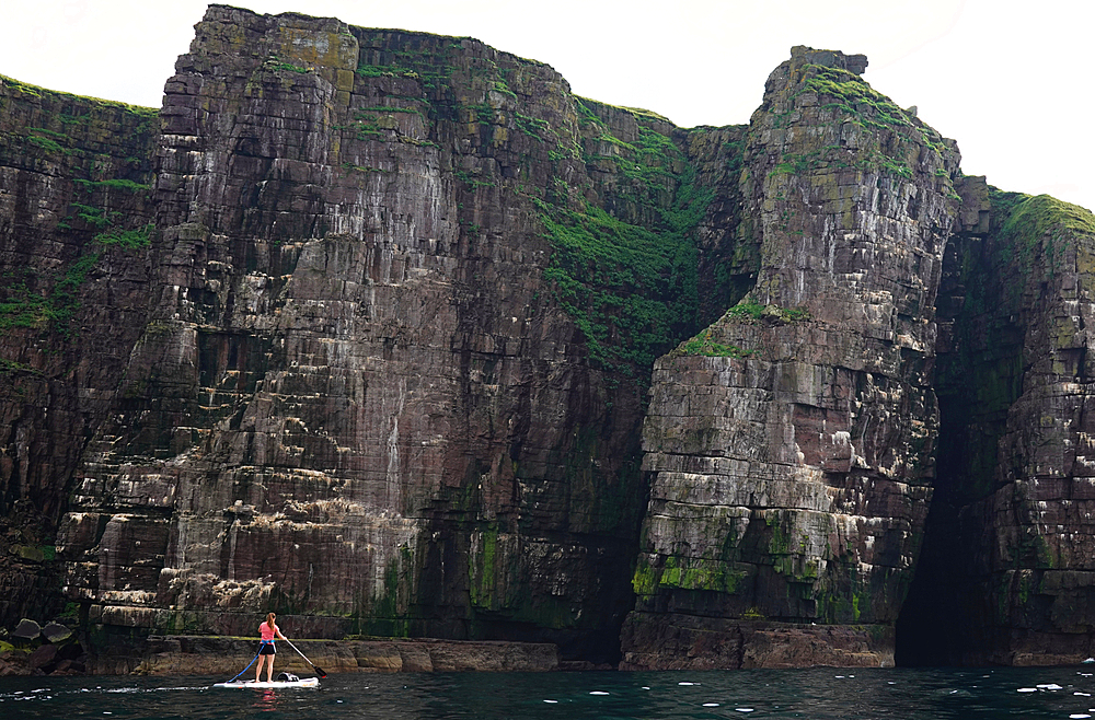 Paddler on a standup paddle board (SUP) off the far northwest coast of Scotland and the cliffs of Handa Island, Sutherland