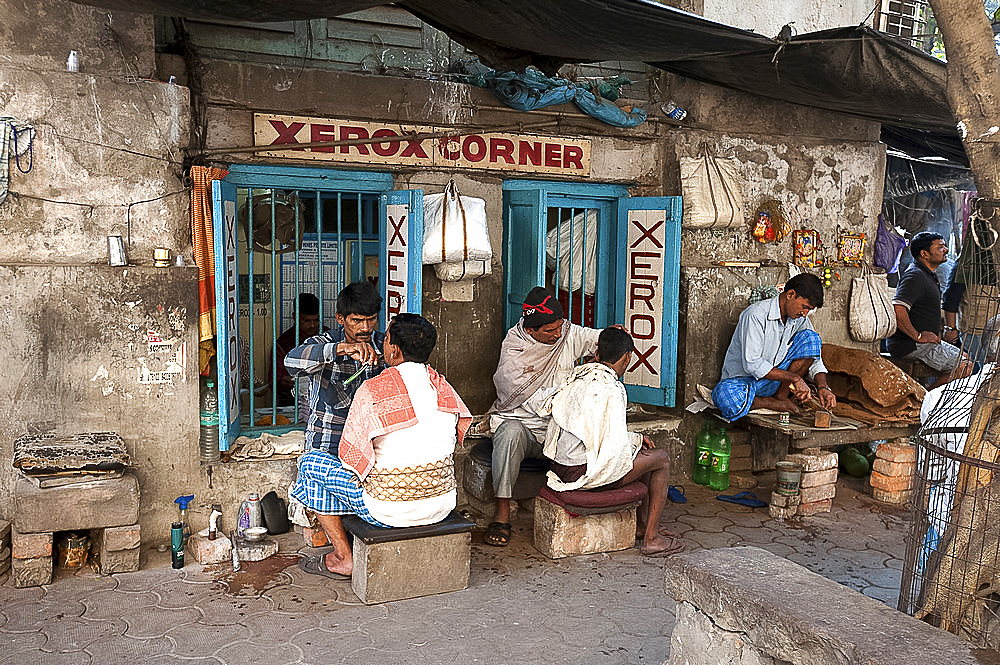 Barbers cutting hair and shaving men, and tobacco wallah, in street stalls outside Xerox shop in Dalhousie Square area of Kolkata (Calcutta), West Bengal, India, Asia