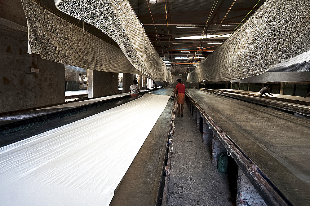 Cotton fabric being prepared on the printing table for screen printing, printed bolts hanging above to dry, Bagru, Rajasthan, India, Asia