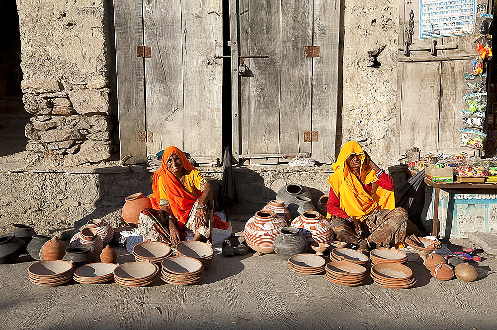 Two women in yellow and orange saris, selling hand made decorated terracotta pots and bowls, Diggi village, Rajasthan, India, Asia