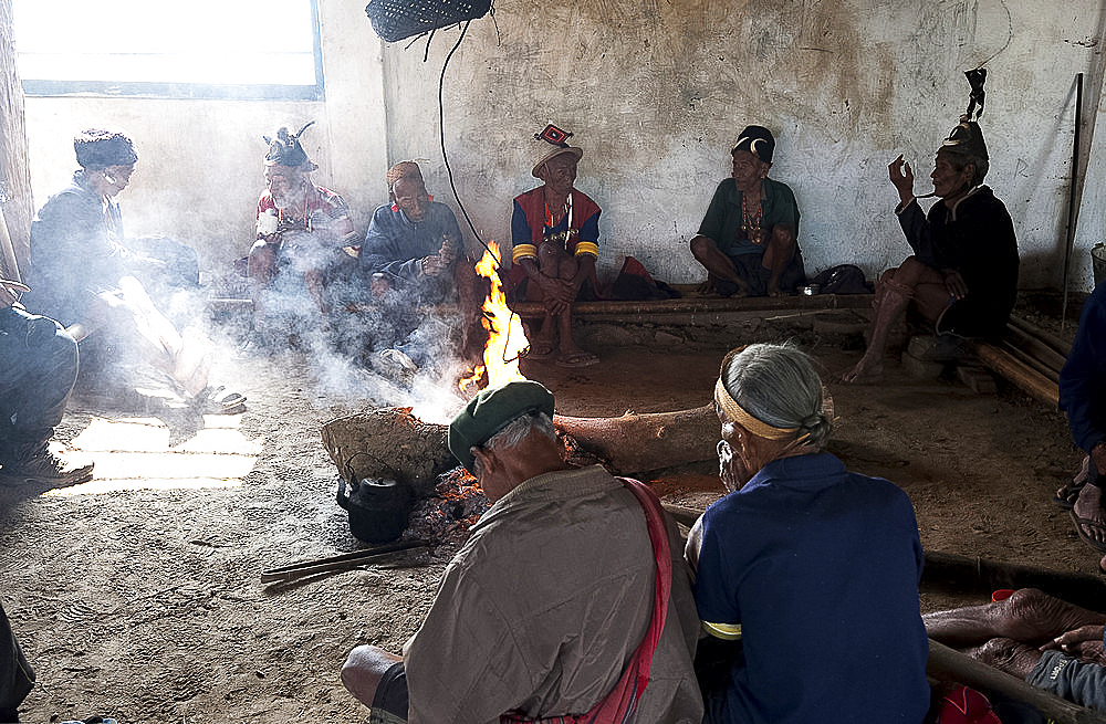 Naga men sitting chatting around the central fire in their village murung (village hall), Hongphui village, Nagaland, India, Asia