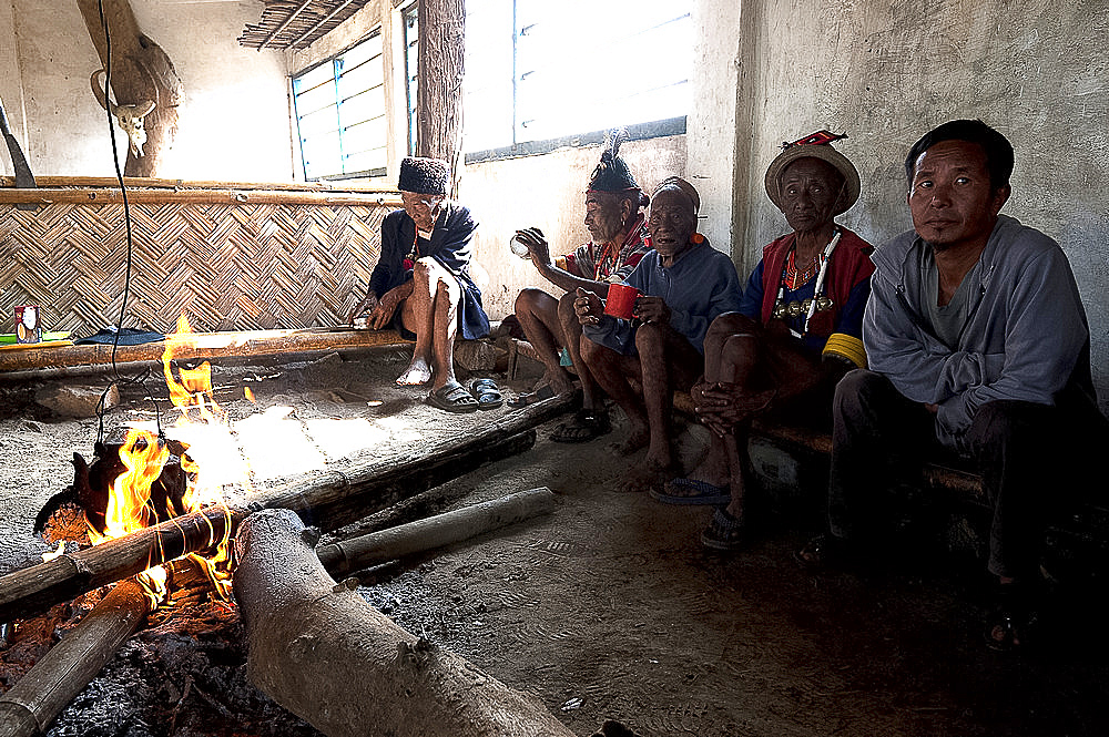 Naga men sitting chatting round fire in village muting (meeting hall), Nagaland, India, Asia