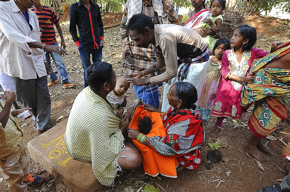 Mali tribeswoman holding hair of child having her head shaved by temple pundit at the festival of Shivraatri, Koraput, Odisha, India, Asia