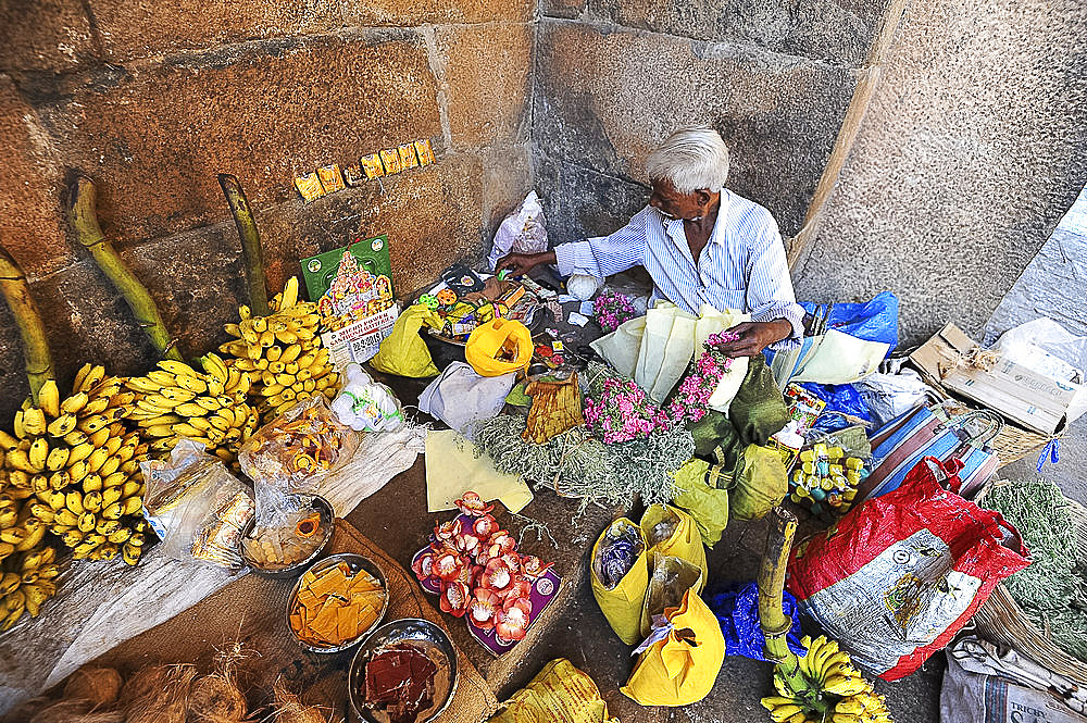 Man preparing puja offerings from flowers, coconuts and fruit in 11th century Brihadisvara temple, Thanjavur, Tamil Nadu, India, Asia