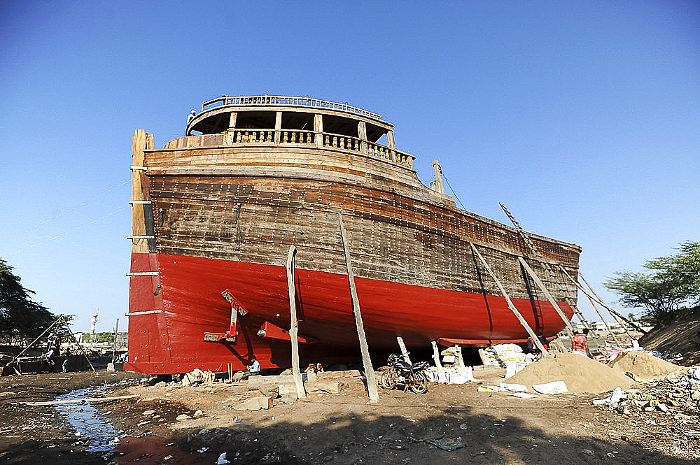 Man putting finishing touches to ocean going dhow at low tide, hand made from Sal wood on the Rukmavati River, Mandvi, Gujarat, India, Asia