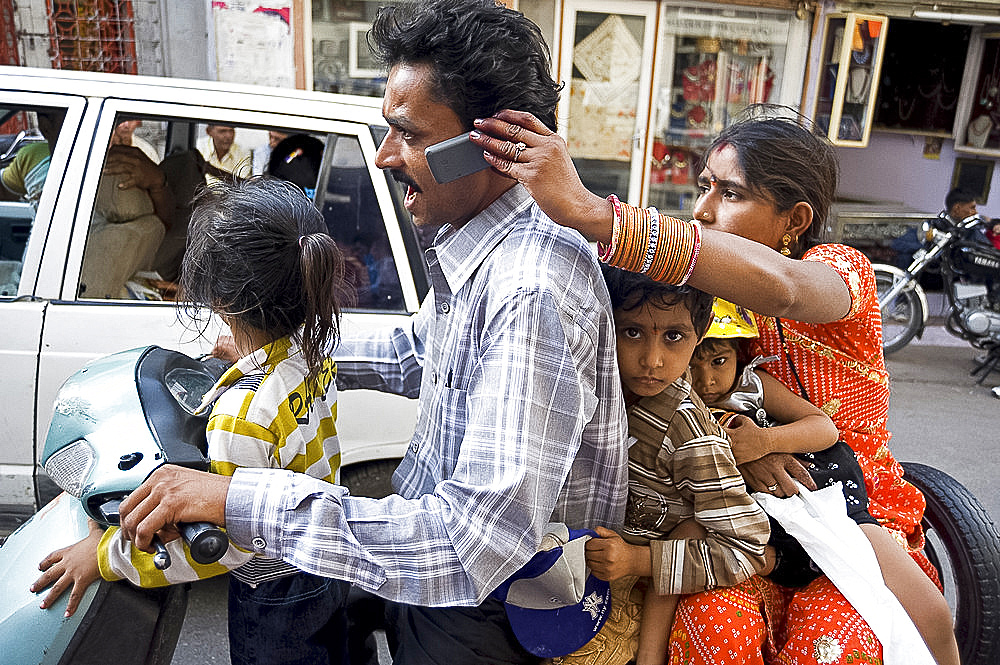 Family of five on scooter, wife holding mobile phone for husband to take call, Udaipur, Rajasthan, India, Asia