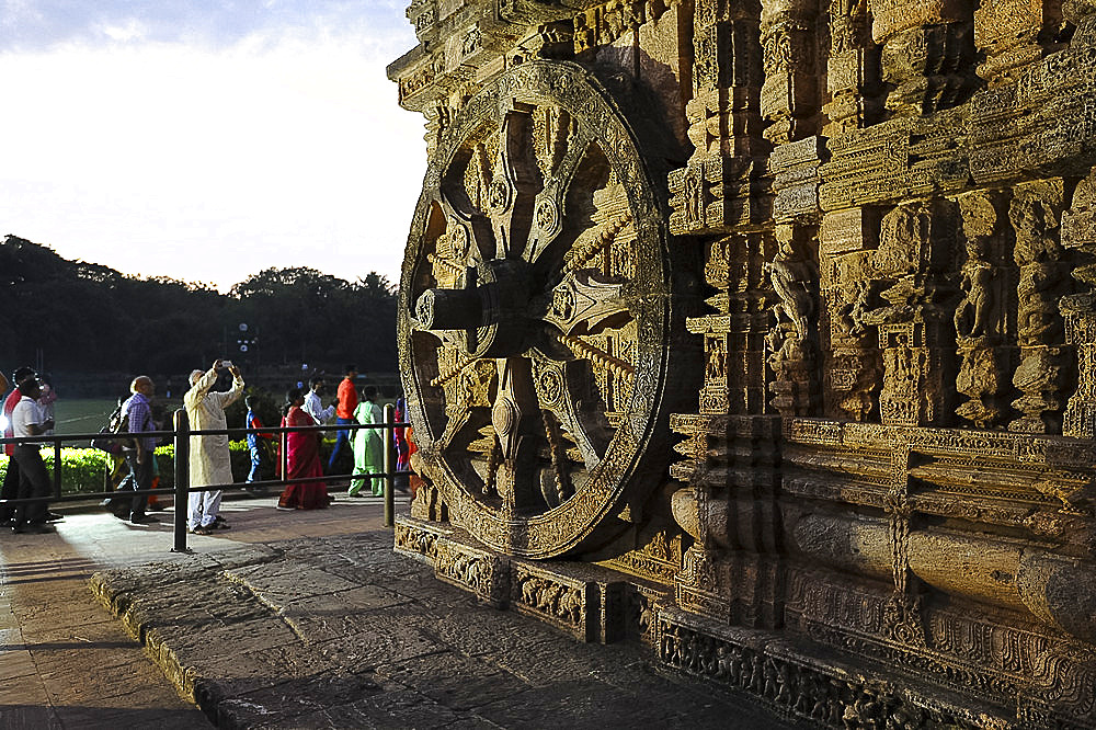 Tourists at sunset by of the 24 carved huge stone chariot wheels carved on 13th century Konark Sun Temple, UNESCO World Heritage Site, Odisha, India, Asia