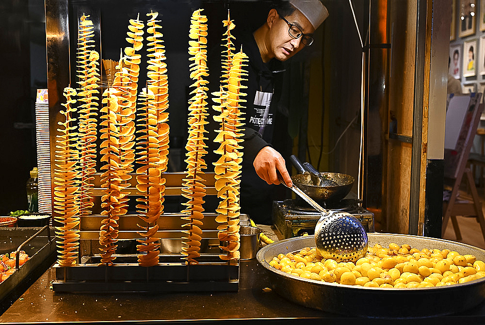 Man cooking fried spiralled potato on long sticks for sale in Muslim quarter night market, Xian, Shaanxi, China, Asia