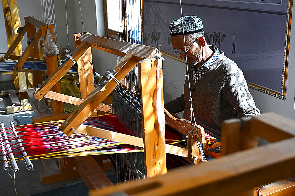 Uyghur man at loom weaving tie dyed silk thread into traditional cloth, Jiya, Xinjiang, China, Asia