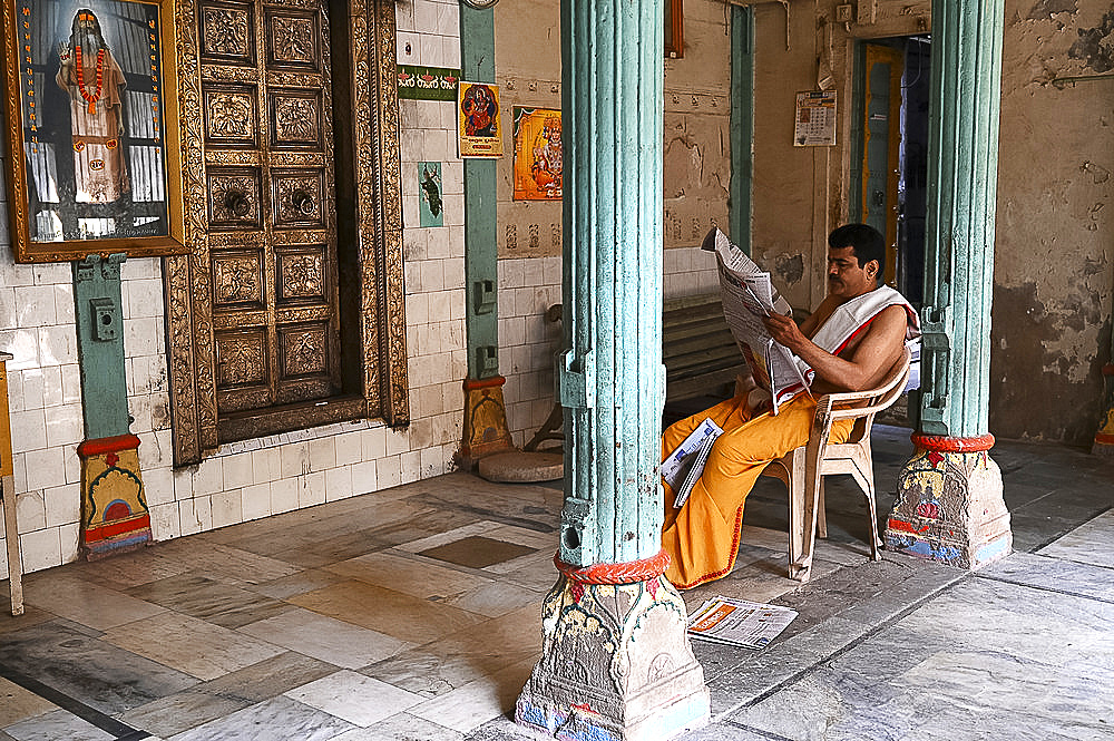 Hindu priest reading the daily newspaper at an old backstreet temple in the palls (alleyways) of old Ahmedabad, Gujarat, India, Asia