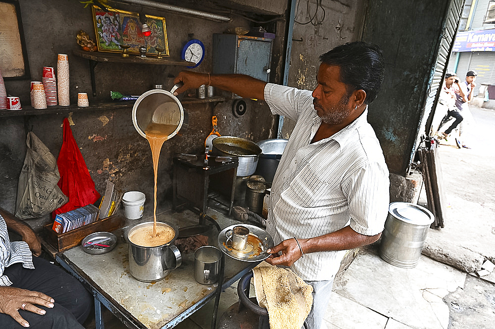 Busy chaiwallah pouring tea at a chai stall in the palls (alleyways) of old Ahmedabad, Gujarat, India, Asia