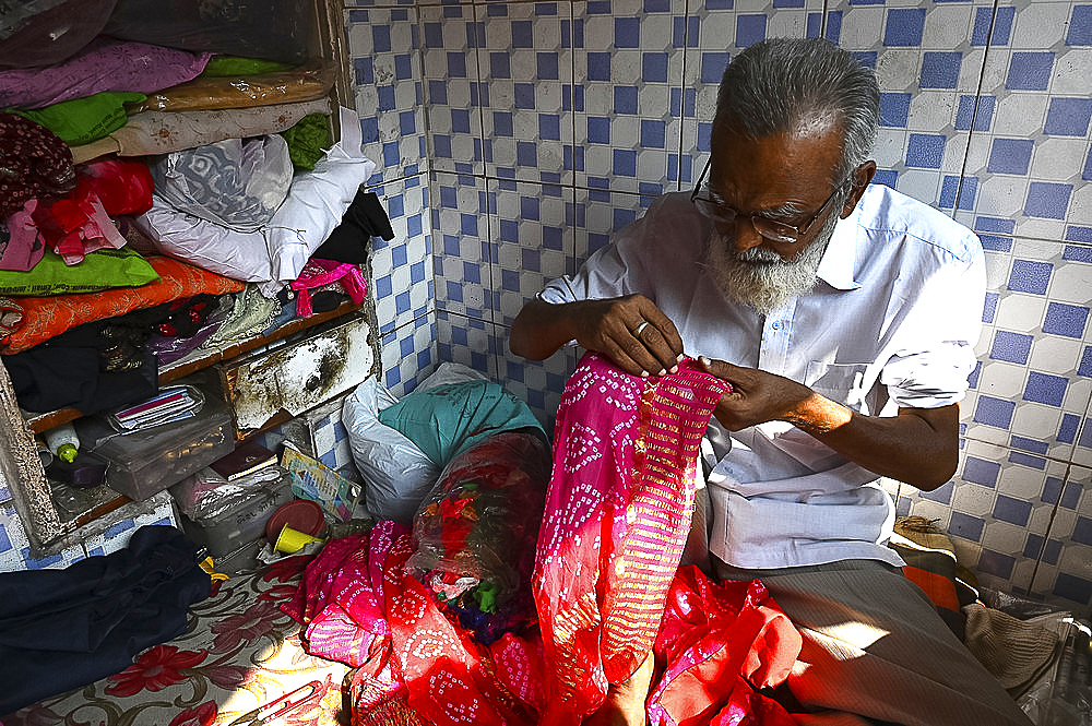 Tailor hand embroidering gold thread onto fabric in his tiny booth in the palls (alleyways) of old Ahmedabad, Gujarat, India, Asia