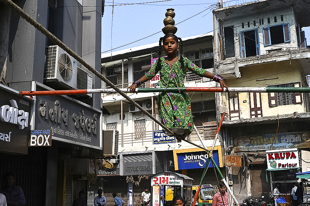 Young girl performing on a tightrope erected in a busy street to earn money, old Ahmedabad, Gujarat, India, Asia