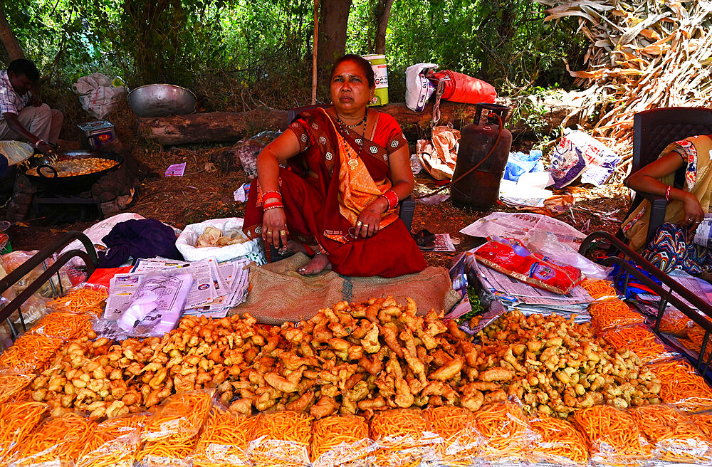 Adivasi woman selling freshly cooked pakora at traditional village fair celebrating Holi festival, Gujarat, India, Asia