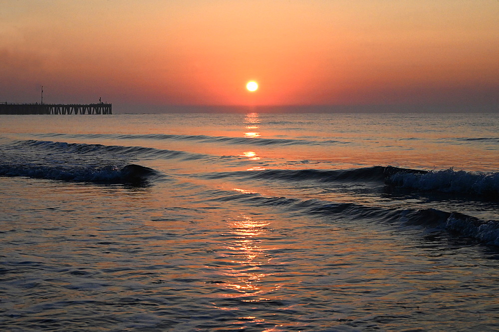 Sunrise over calm sea silhouetting the old derelict harbour wall and groyne, Walberswick, Suffolk, England, United Kingdom, Europe