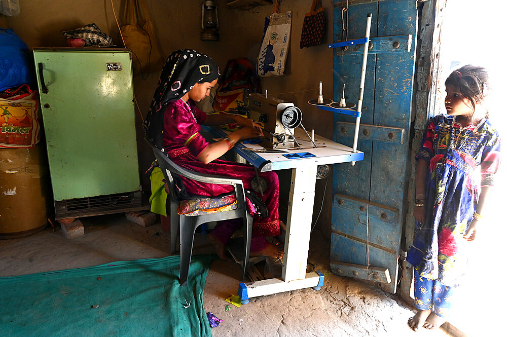 Two tribal village girls, one making traditional quilt using sewing machine in village house, Kachchh desert area, Gujarat, India, Asia