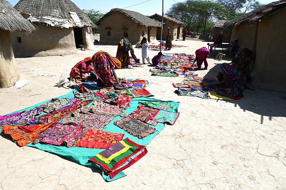 Tribal village women laying out their tribal embroidery outside mud walled houses in their tribal village, Kachchh, Gujarat, India, Asia