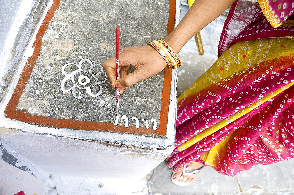 Woman painting her doorstep with rice flour paste, making rangoli design Diwali Festival decorations, Udaipur, Rajasthan, India