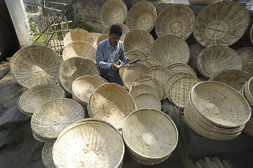 Basketmaker reading newspaper whilst waiting for customers in early morning market on the banks of the Brahmaputra river, Guwahati, Assam, India, Asia