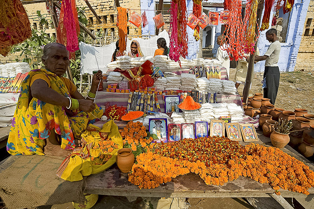 Woman selling marigold mala (garlands), pictures of Hindu deities, agarbathi (joss sticks) and rolimoli temple threads from stall at Sonepur Cattle Fair, near Patna, Bihar, India, Asia