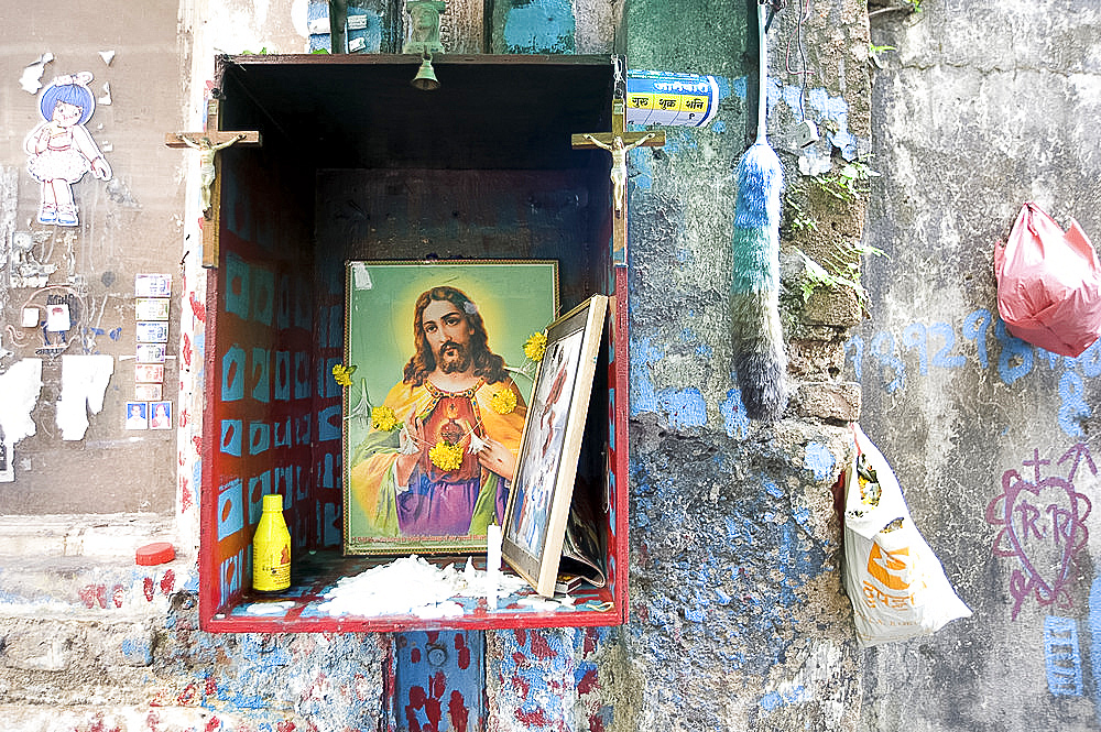 Christian shrine in wooden box on a street wall, with candle, marigolds and offerings, Colaba back street, Mumbai, India, Asia