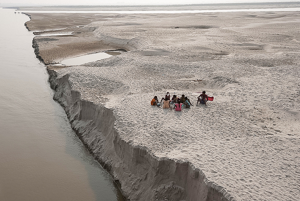 Villagers stopping to eat near the fragile edge of a sandspit in the River Ganges, Sonepur, Bihar, India, Asia