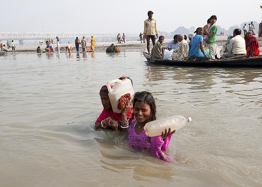 Mother and daughter wading across the River Ganges holding bottles of Holy River Ganges water, Sonepur, Bihar, India, Asia