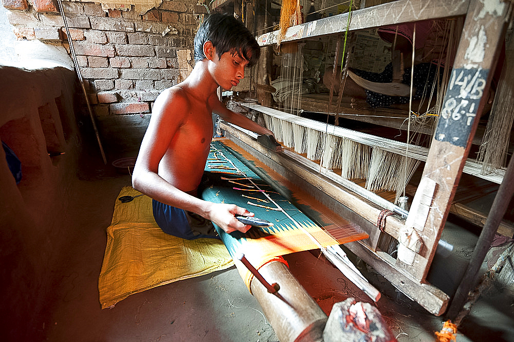 Young boy at domestic loom weaving patterned silk sari using several spools of silk, Vaidyanathpur weaving village, Orissa, India, Asia