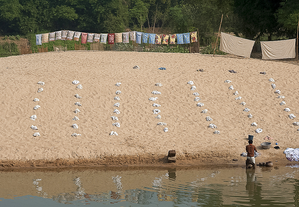 Dhobi wallah washing laundry in the river with very organised piles of white washing laid out on the sand, Raghurajpur, Orissa, India, Asia