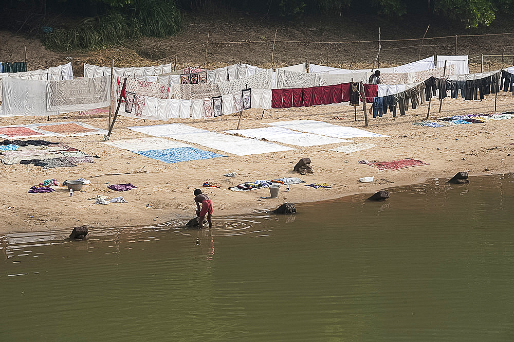 Dhobi wallah washing laundry in the river with neatly arranged washing drying on the sandy riverbank, Raghurajpur, Orissa, India, Asia