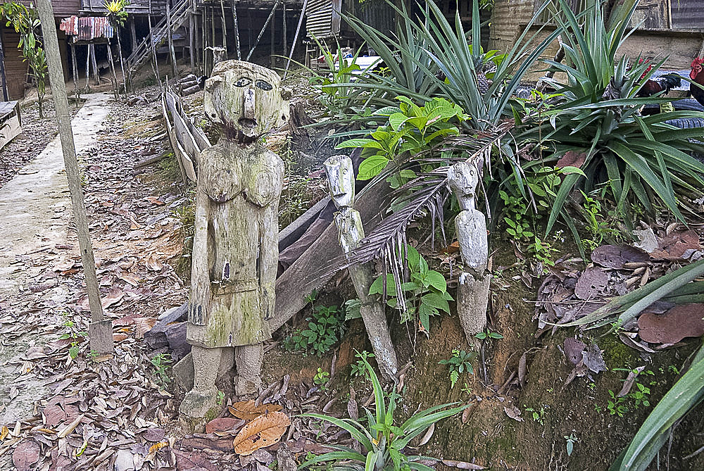 Carved spirits of men and a woman standing at the entrance to Iban tribal longhouse at Ngemah beach on the Lemanak River, Sarawak, Malaysian Borneo, Malaysia, Southeast Asia, Asia