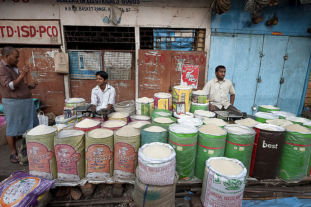 Rice wallahs sitting behind full sacks of rice waiting for customers in the early morning, New Market, Kolkata, West Bengal, India, Asia